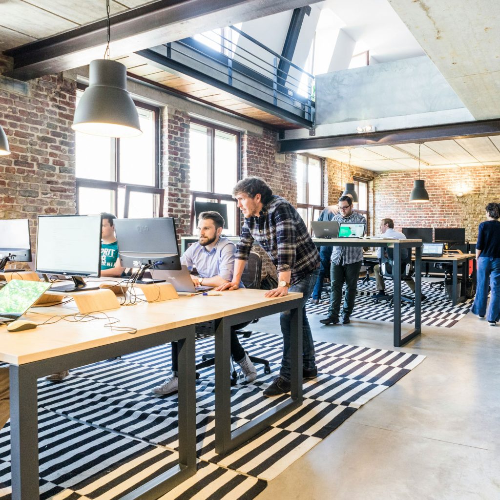 Mitarbeiter in einem lichtdurchfluteten Büro am Computer oder im Gespräch miteinander