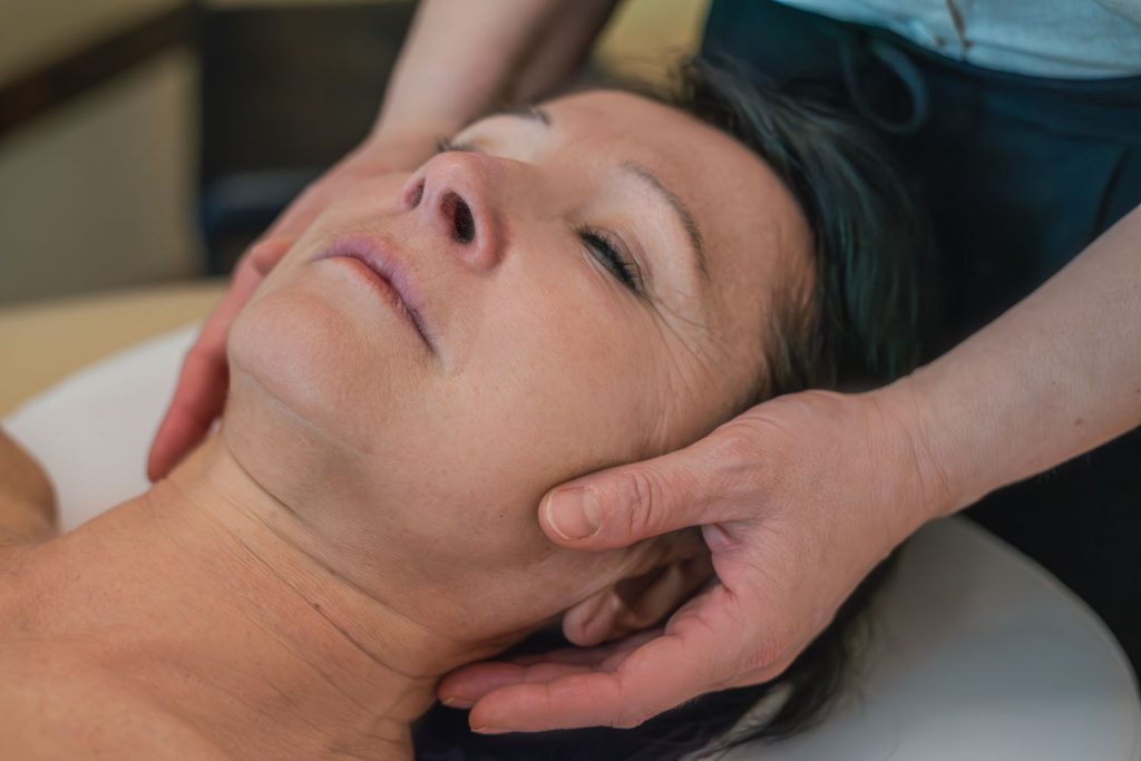 Susan Mehr massiert mit sanften Streichbewegungen den Kiefer einer älteren Kundin während der Anti-Stress-Massage
