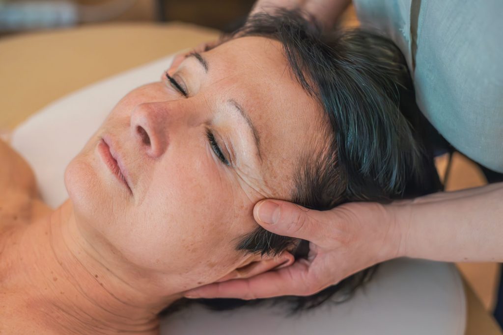 Susan Mehr massiert mit den Daumen die Schläfen einer Kundin während der Gesichts- und Kopfmassage