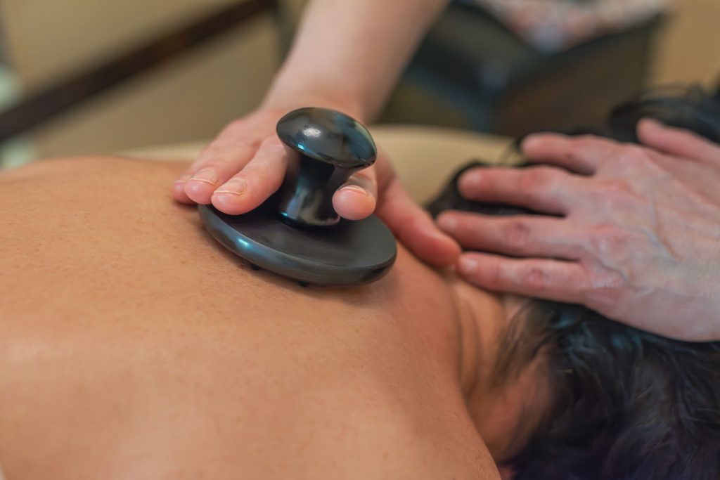 Als Teil der Cellulitemassage behandelt Susan Mehr den oberen Rücken einer auf dem Bauch liegenden Kundin mittels eines Ebonit-Instruments