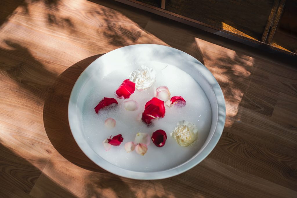 Weiße Porzellanschüssel mit Schaumbad und Rosenblüten