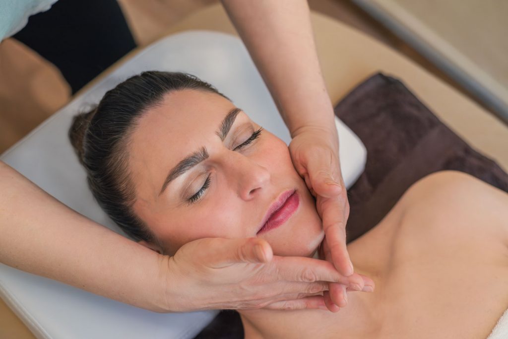 Susan Mehr massiert mit sanften Streichbewegungen den Kieferbereich einer Kundin während der Aromaölmassage