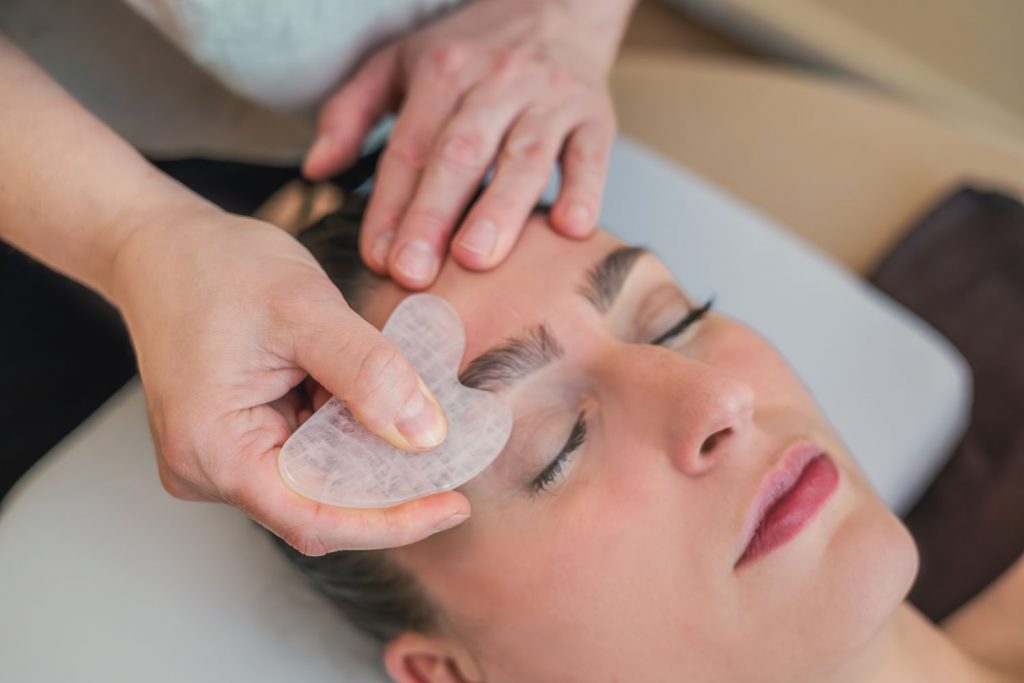 Mittels Gua Sha massiert Susan Mehr den Bereich der Augenbraue einer Kundin während der Gesichts- und Kopfmassage