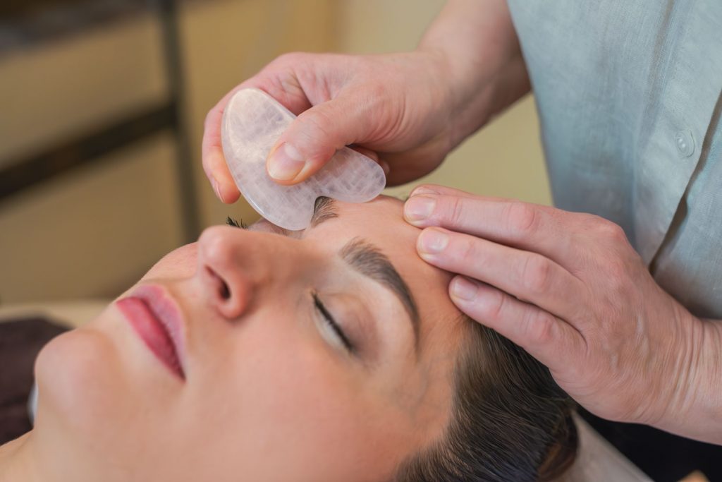 Für eine vollständige Entspannung behandelt Susan Mehr den Bereich der Augenbraue einer Kundin mit Gua Sha während der Anti-Stress-Massage