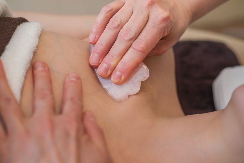 Der Bereich zwischen Brust und Schulter wird sanft mit einem rosafarbenen Gua Sha Stein massiert