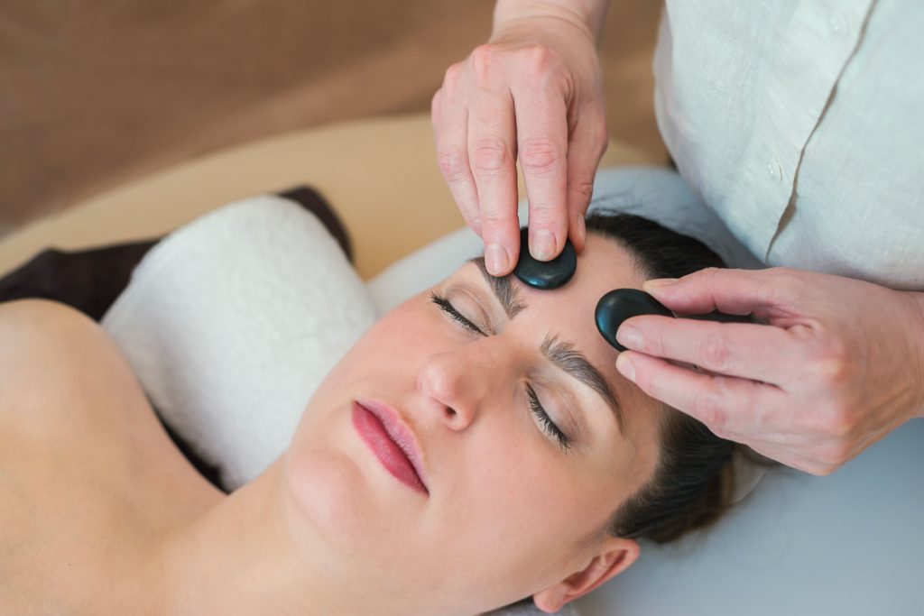 Susan Mehr behandelt mittels kleiner warmer Steine die Stirn einer Kundin im Rahmen der Hot-Stone-Massage