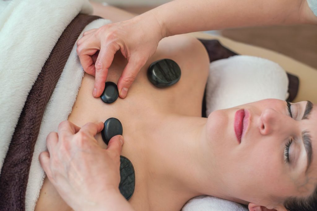 Susan Mehr platziert zusätzlich zu zwei großen schwarzen Steinen zwei kleine Steine entlang der Schlüsselbeinlinie als Teil der Hot-Stone-Massage