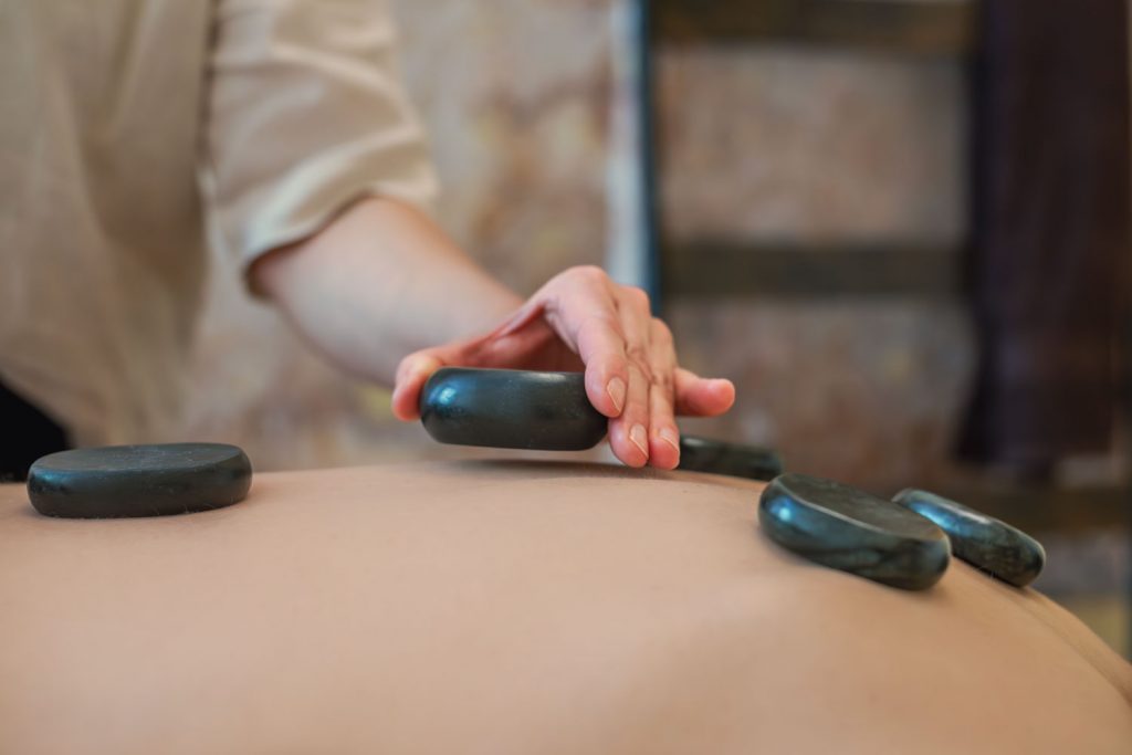 Susan Mehr platziert angenehm warme Steine auf dem Rücken einer Kundin im Rahmen der Hot-Stone-Massage
