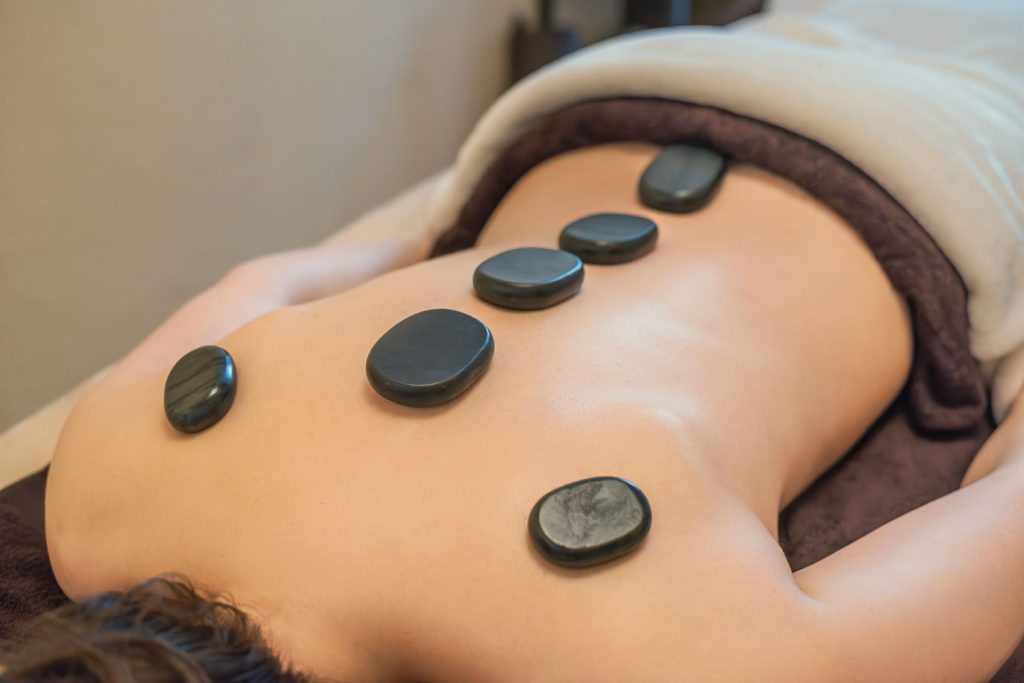 Als Teil der Hot-Stone-Massage liegen sechs warme Steine entlang der Wirbelsäule und auf den Schulterblättern einer Kundin, die entspannt auf dem Bauch liegt