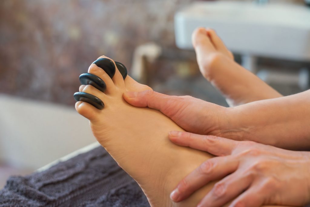 Im Rahmen der Hot-Stone-Massage werden die Füße einer Kundin massiert, zwischen deren Zehen kleine warme Steine stecken