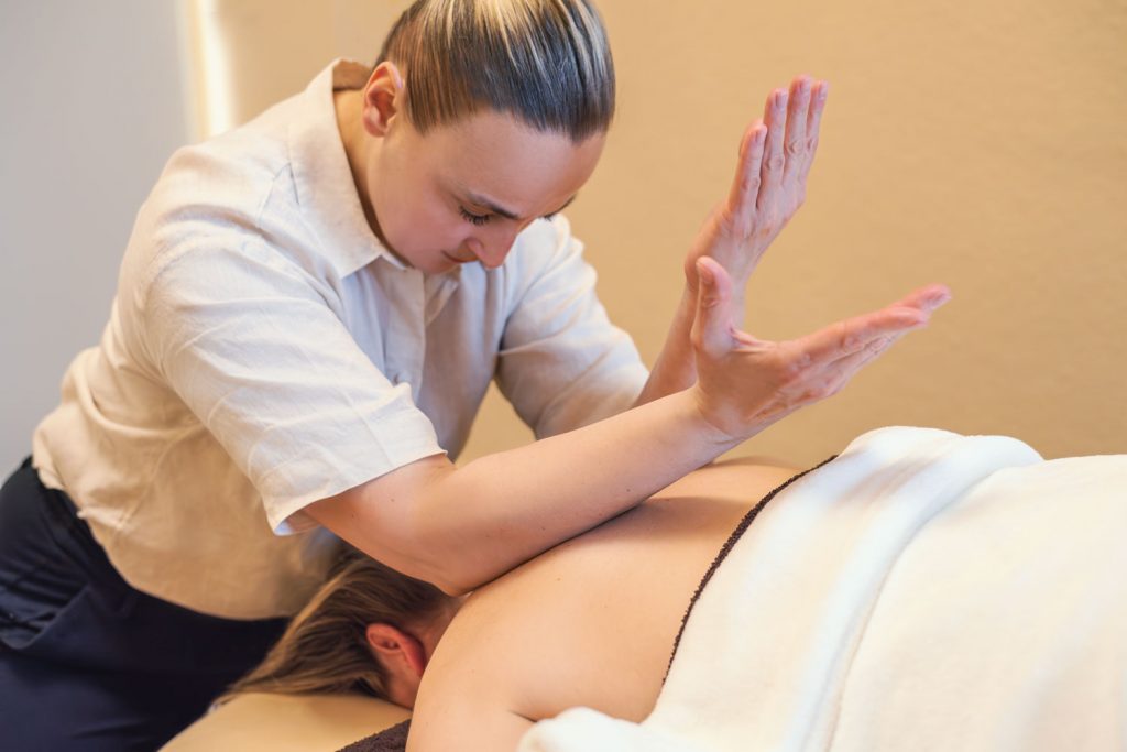 Mit den Ellbogen und Unterarmen löst Susan Mehr Verspannungen einer Kundin im Nacken und Schulterbereich während der Teilkörpermassage