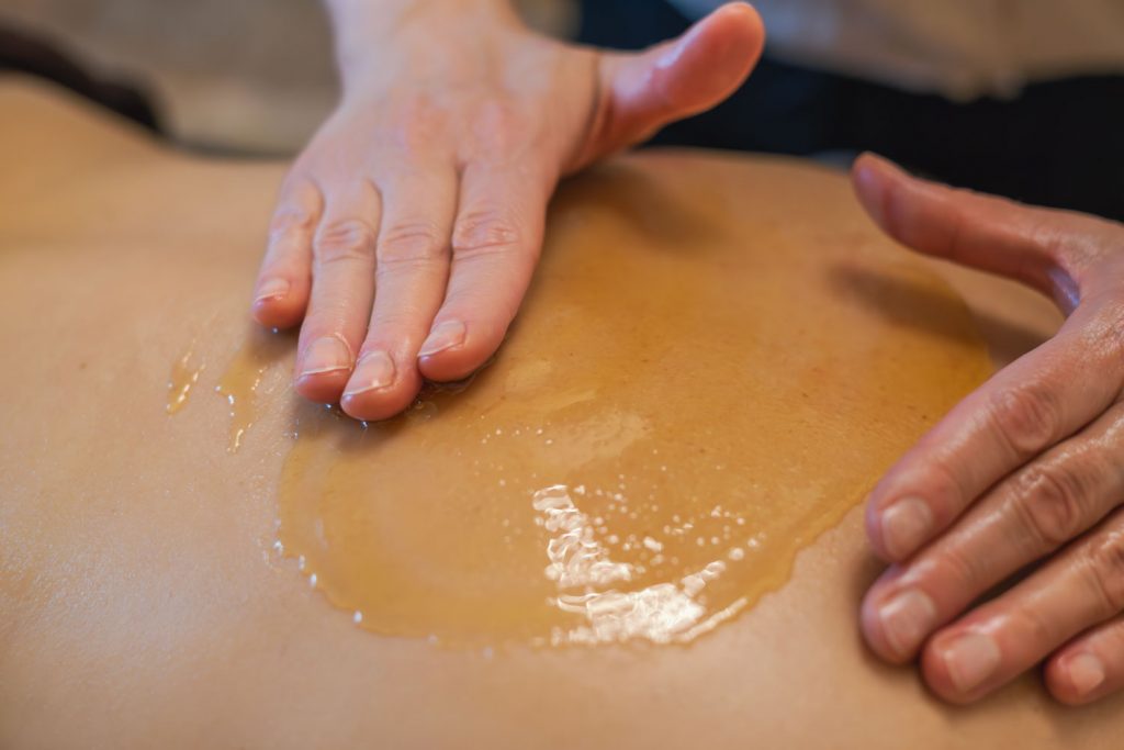 Susan Mehr verteilt in sanften Kreisbewegungen den Honig auf dem Rücken einer Kundin zu beginn der Honigmassage